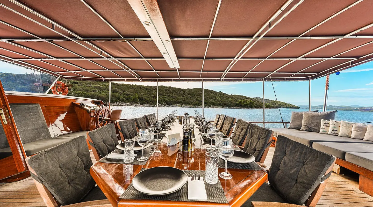 Luxurious sailing yacht dining area under shade, wooden table set for meals