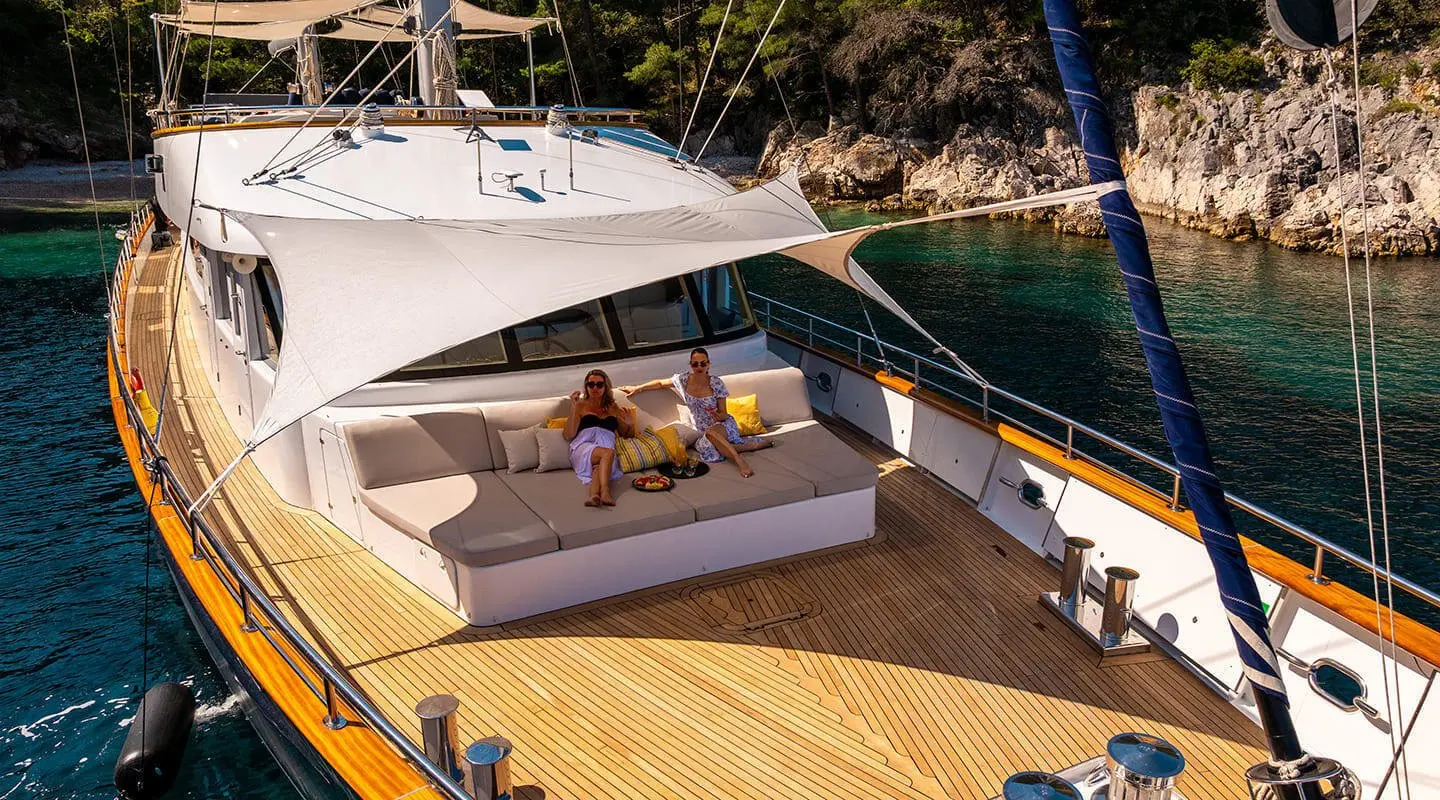 Two people lounging on a white cushioned sofa on the yacht's teak deck