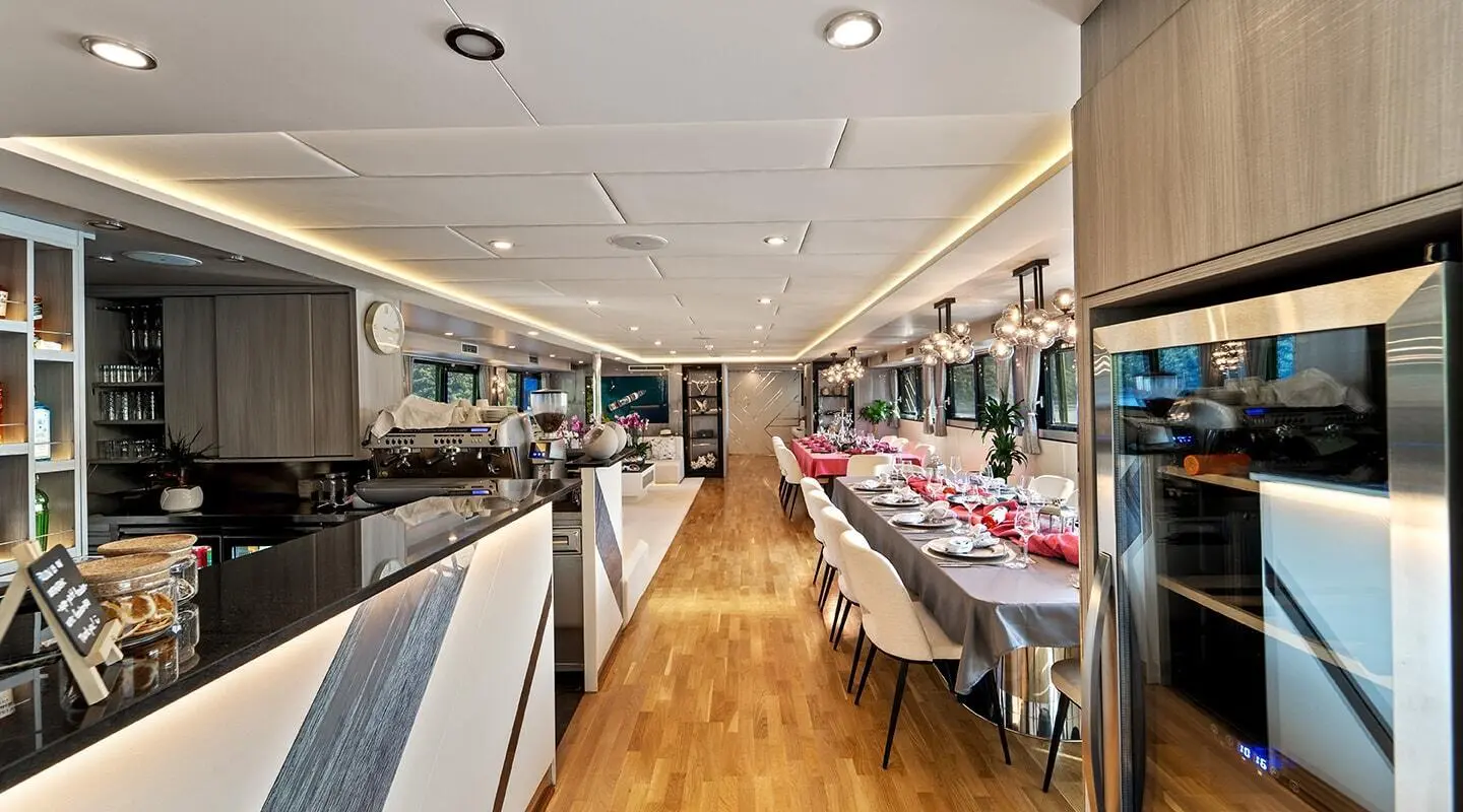 Interior of a yacht with a long dining table set for a meal and a bar area
