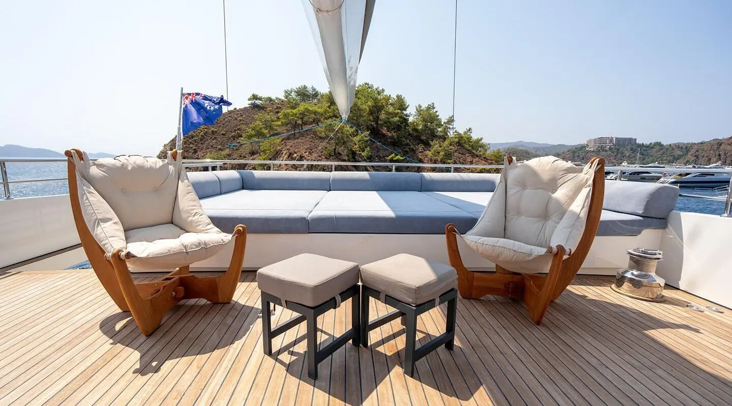Sunlit deck with two cushioned chairs and small stools, open sea view