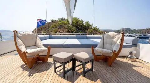 Sunlit deck with two cushioned chairs and small stools, open sea view
