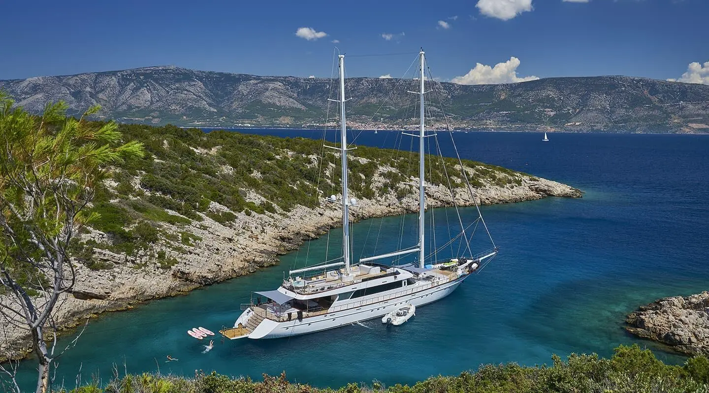 Yacht Lady Gita anchored in turquoise cove with rocky coastline