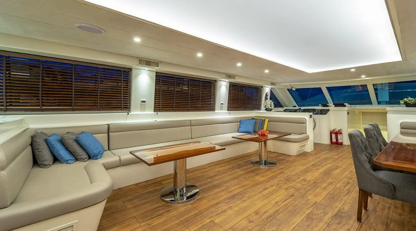 Queen Of Makri yacht deck seating area with wooden floor and white cushions at sunset