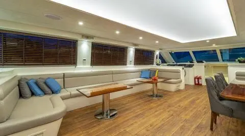 Queen Of Makri yacht deck seating area with wooden floor and white cushions at sunset