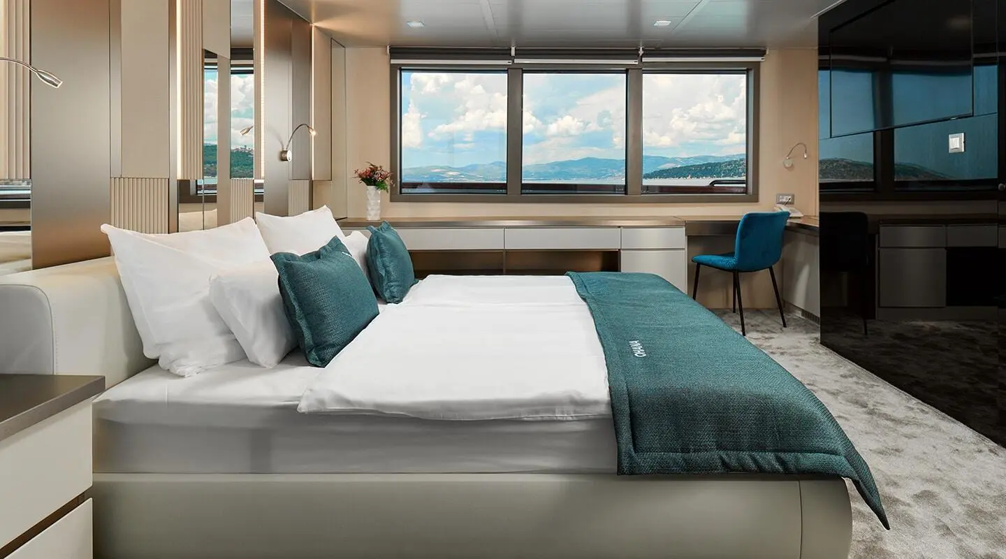 Ohana master cabin aboard yacht with a large bed, teal textiles, and windows