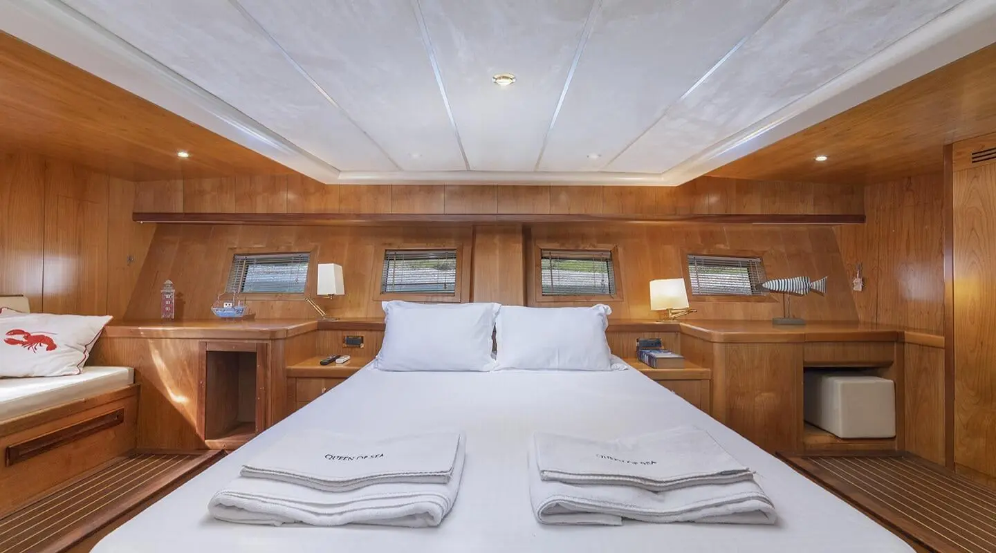 Queen Of Sea yacht interior with a large bed, wooden panels, and porthole windows at sunset