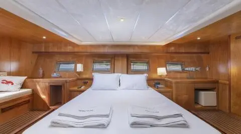Queen Of Sea yacht interior with a large bed, wooden panels, and porthole windows at sunset