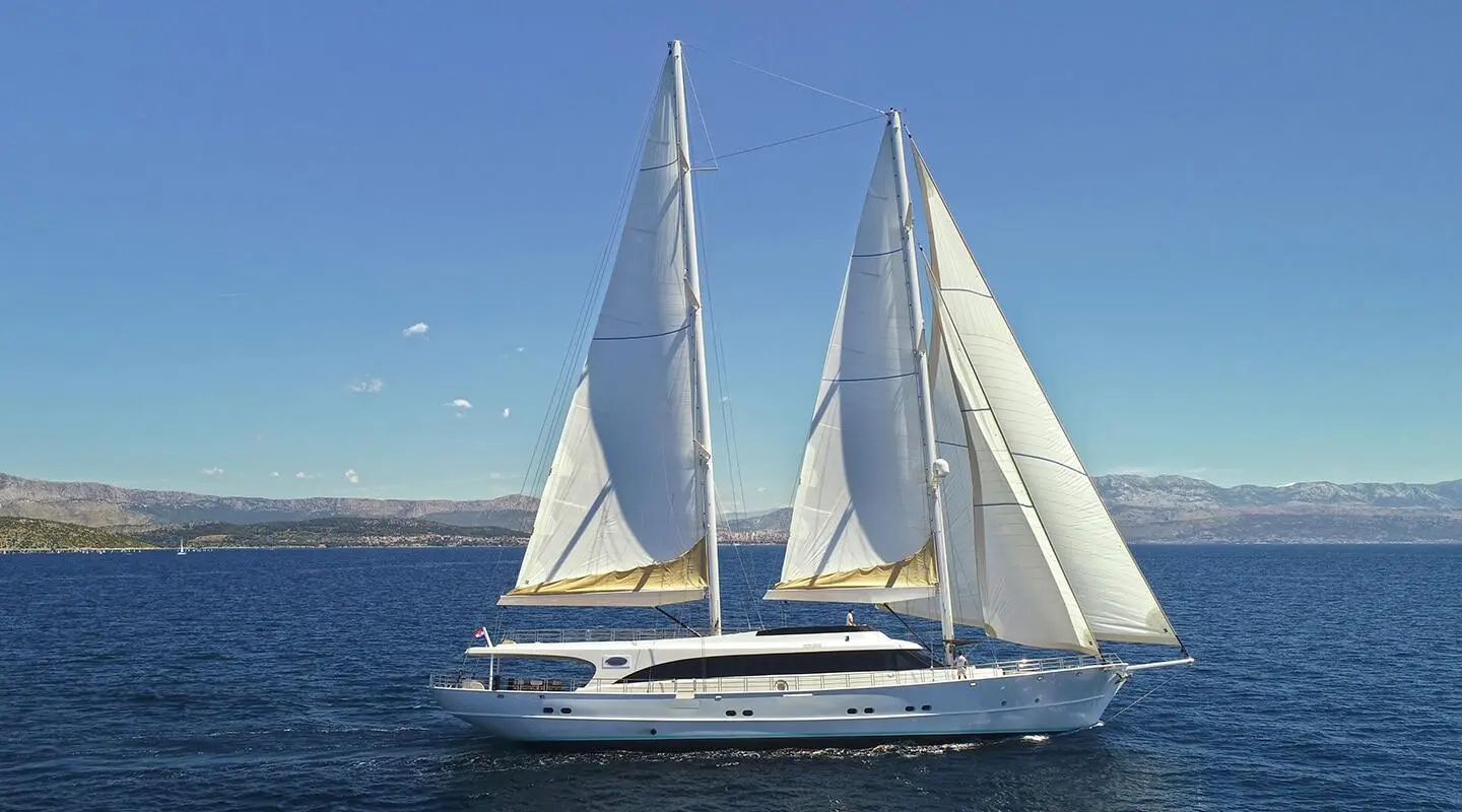 Sleek motor yacht Acapella sails with two tall white masts on calm blue sea
