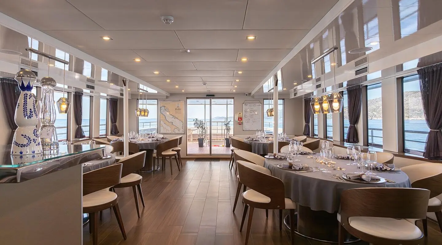 Dining salon with round tables set, windows and sea view