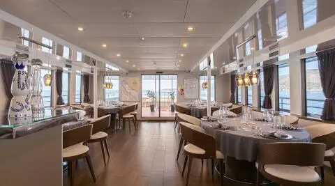 Dining salon with round tables set, windows and sea view