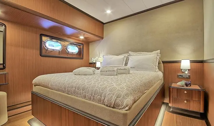 Queen Of Salmakis cabin with king bed, neutral tones, wood shelving, porthole view