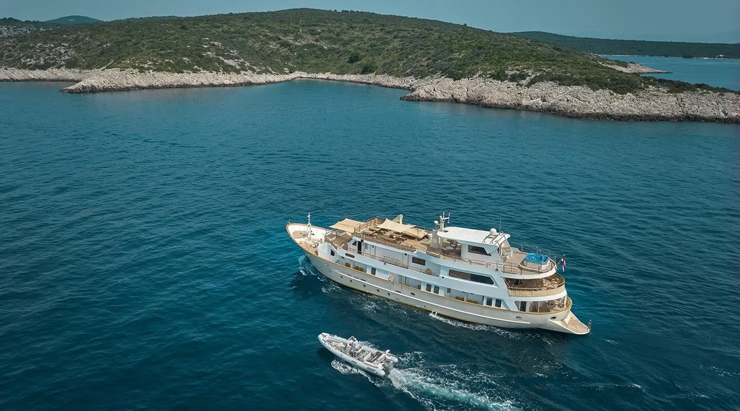 Luxurious yacht La Perla sailing on blue sea with rocky coastline in the background