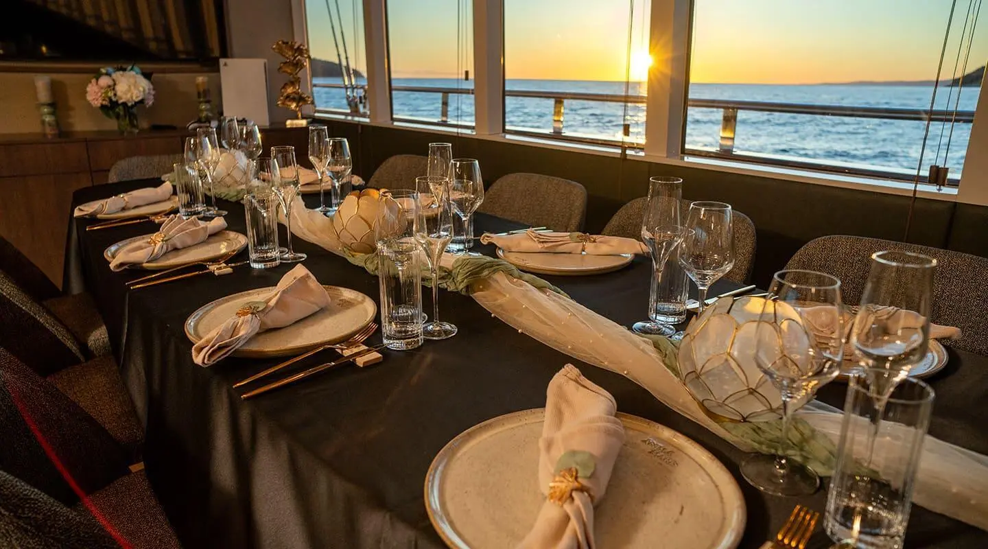 Luxurious yacht dining setup aboard Anima Maris with sunset views through windows