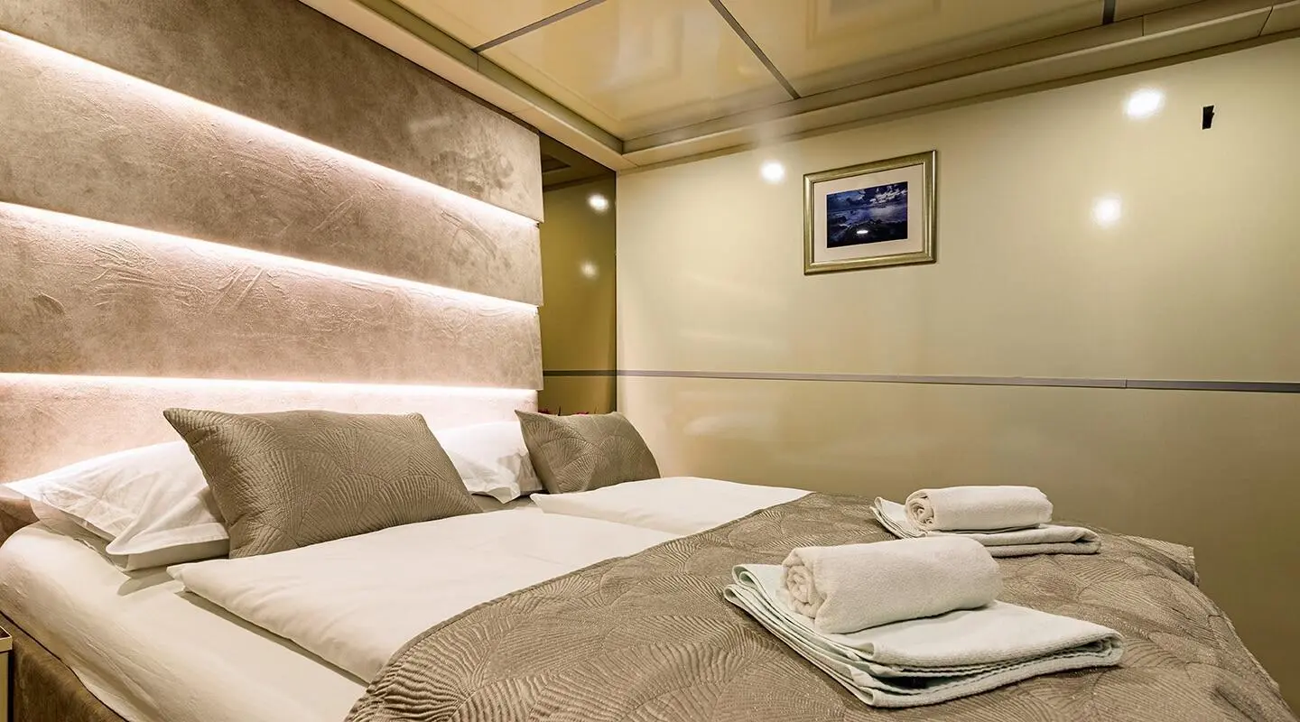 Melody yacht cabin with plush bed, beige headboard, and folded towels on the bed