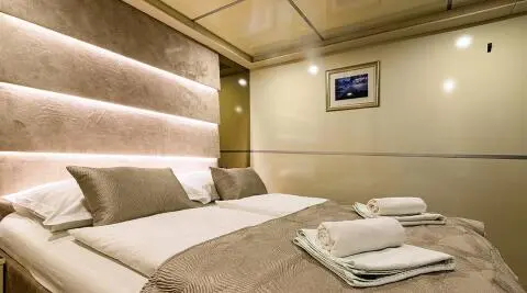 Melody yacht cabin with plush bed, beige headboard, and folded towels on the bed