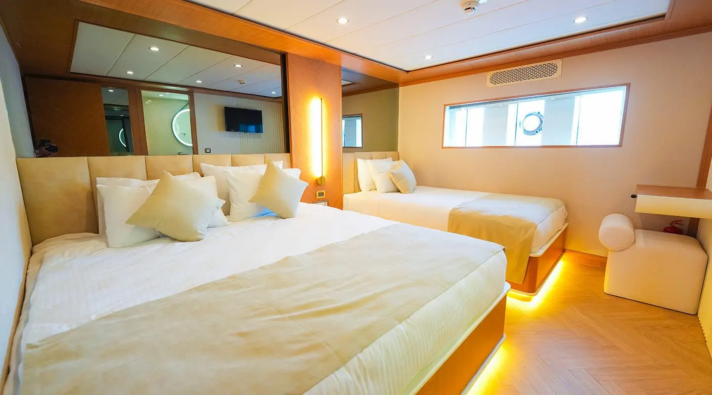 Luxurious yacht cabin with two beds, warm lighting, wooden accents, and porthole window