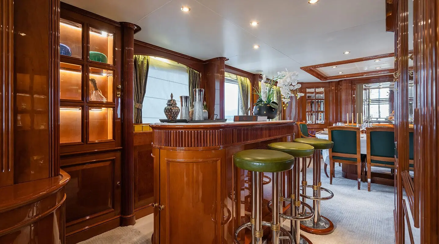 Amadea yacht interior bar with polished wood, green stools, and dining area