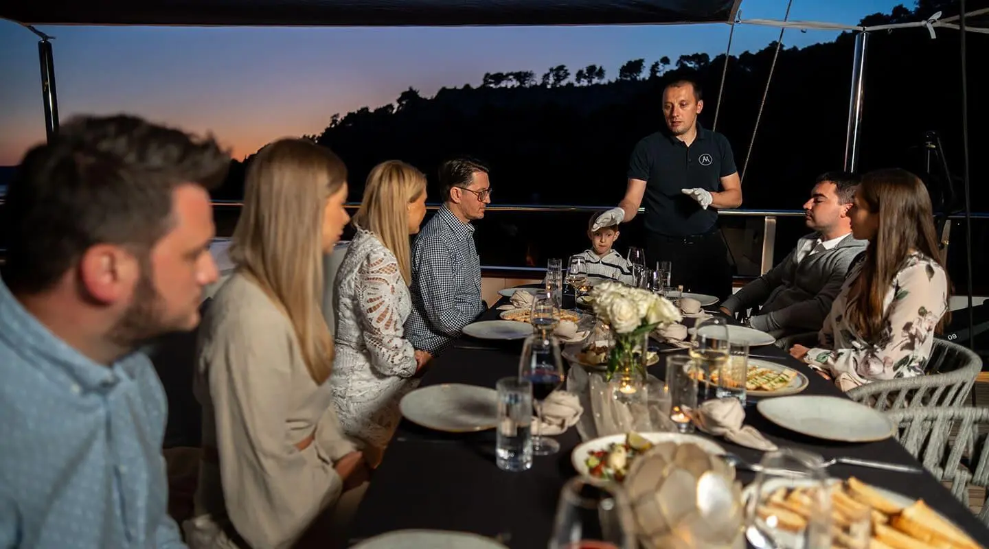 Yacht Anima Maris with guests at an outdoor dining table during sunset