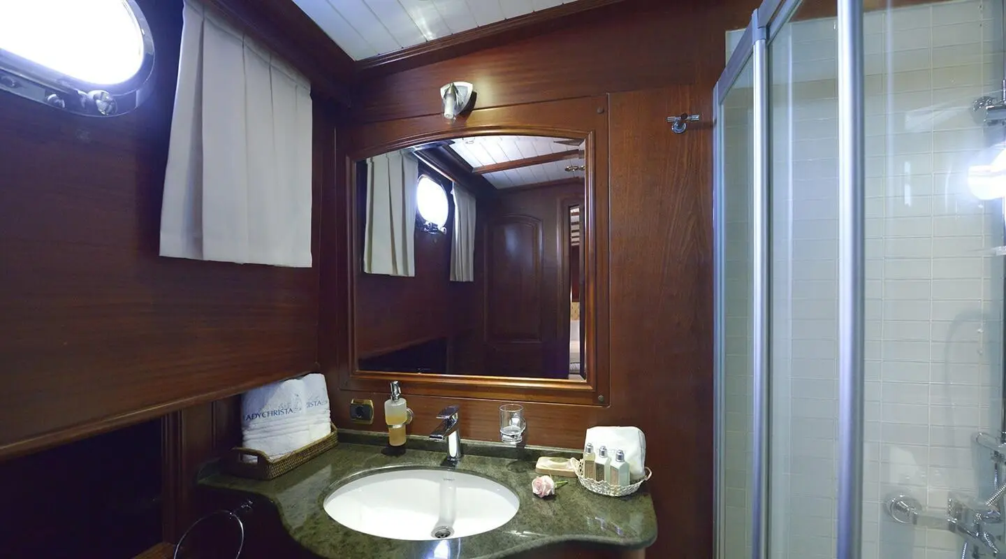 Lady Christa yacht bathroom with dark wood paneling, oval sink, and glass shower enclosure
