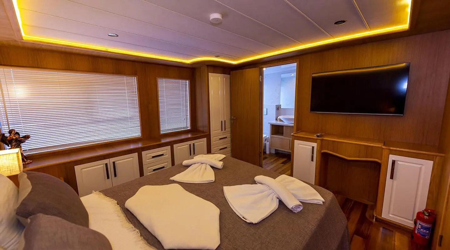 Interior view of a luxurious yacht cabin with bed, seating, and wooden paneling