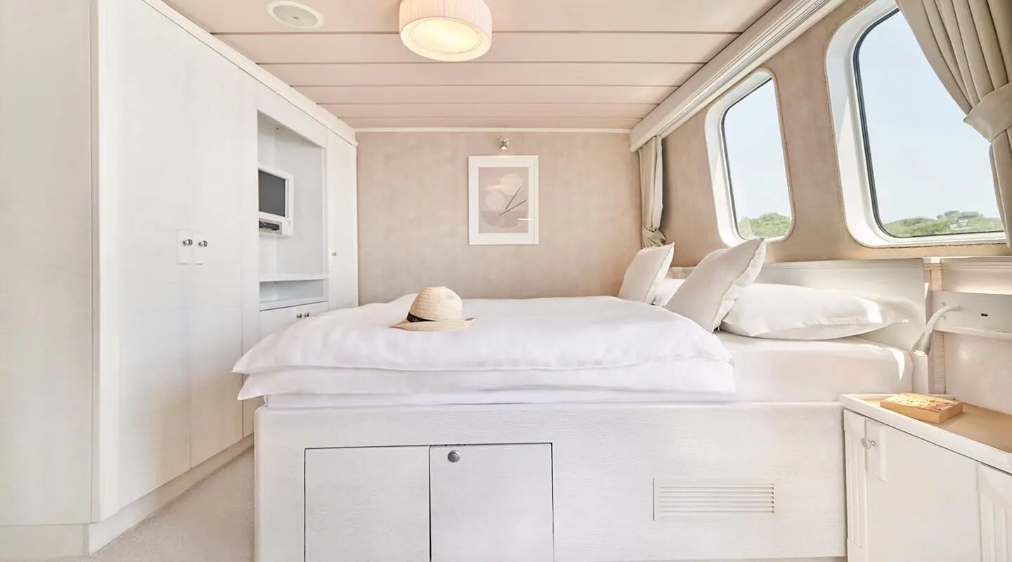 La Perla yacht villa-style cabin with white bed and sunlit windows