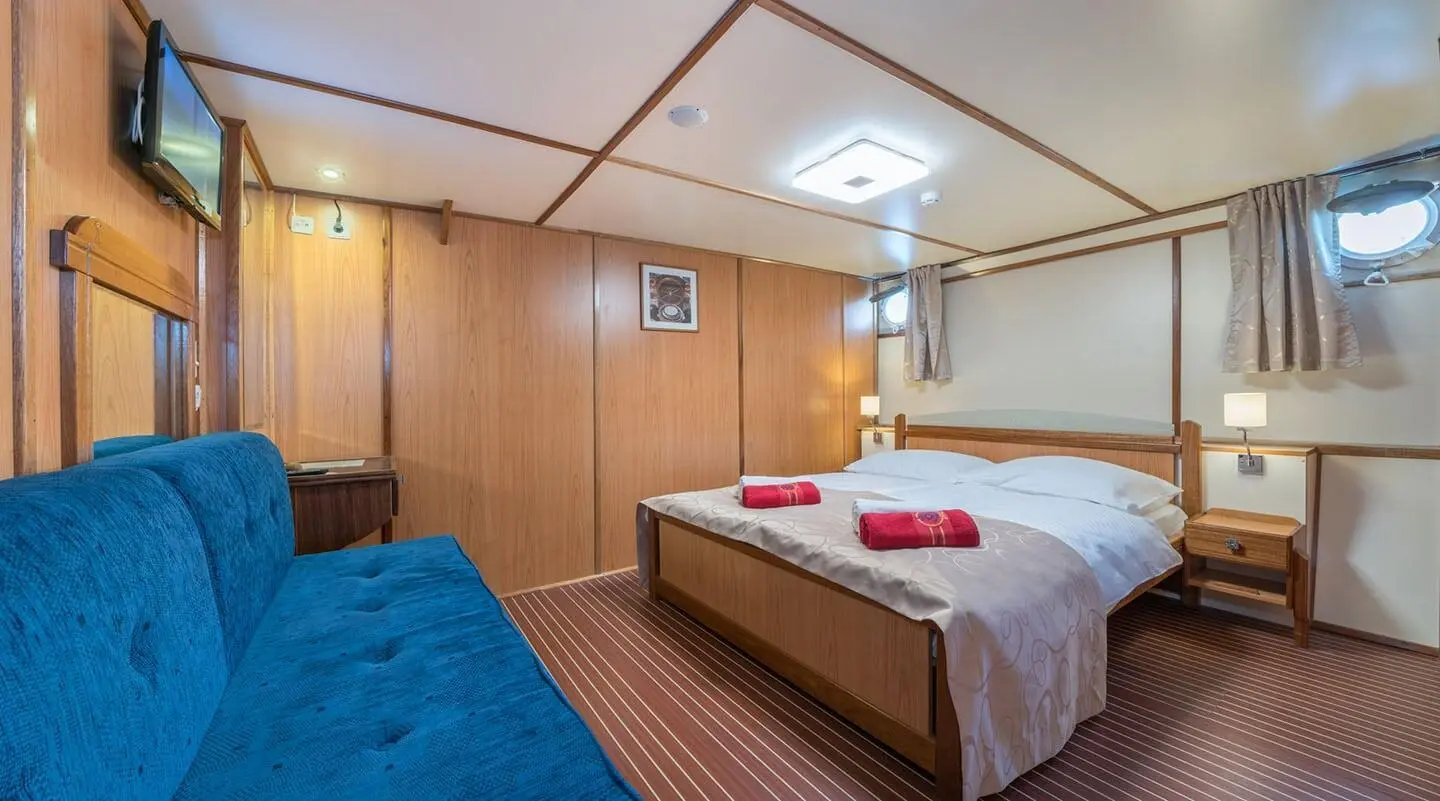 Interior of Barbara yacht with a bed, wooden paneling, and porthole window
