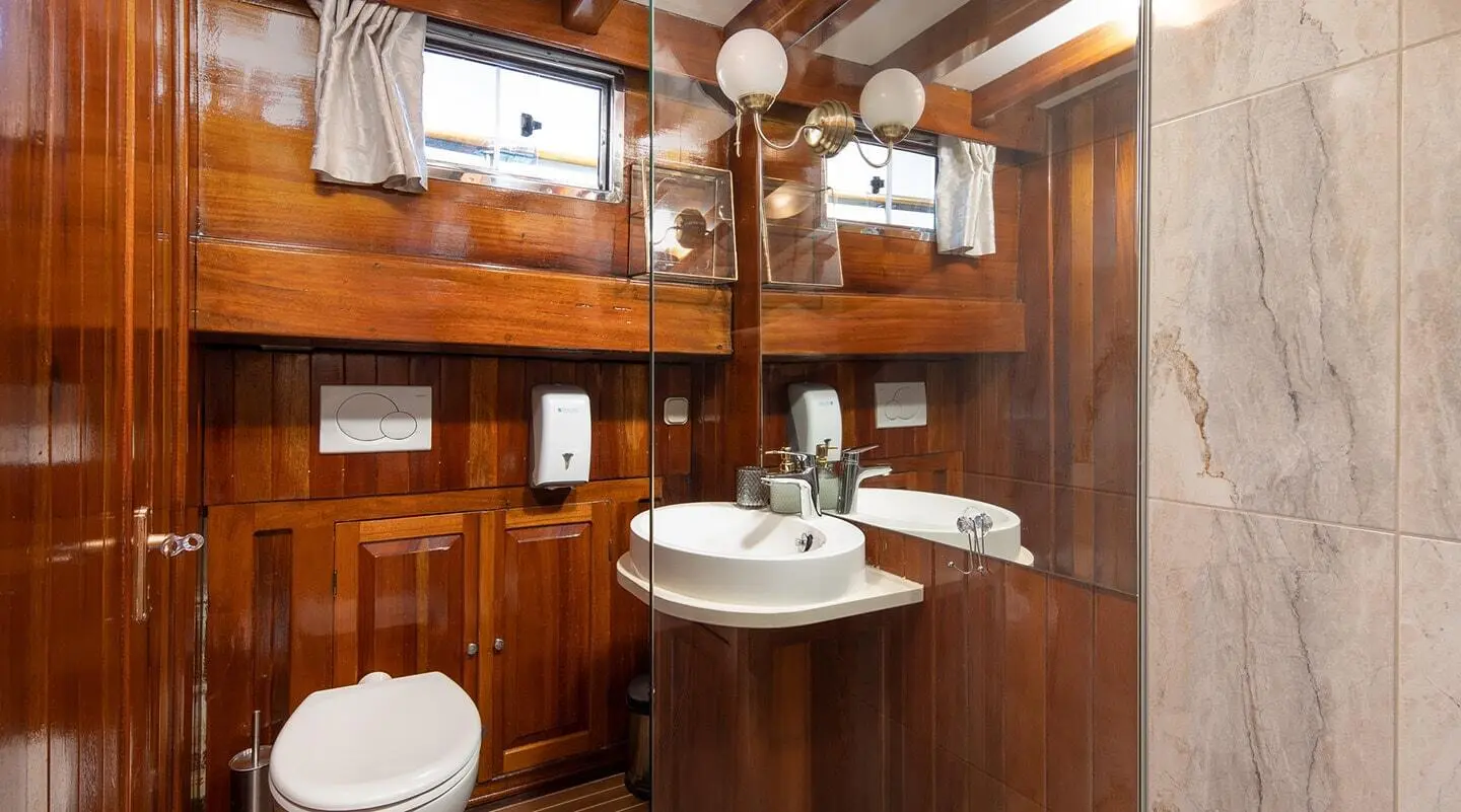 Interior shot of a wooden yacht bathroom with sink, mirror, and porthole.