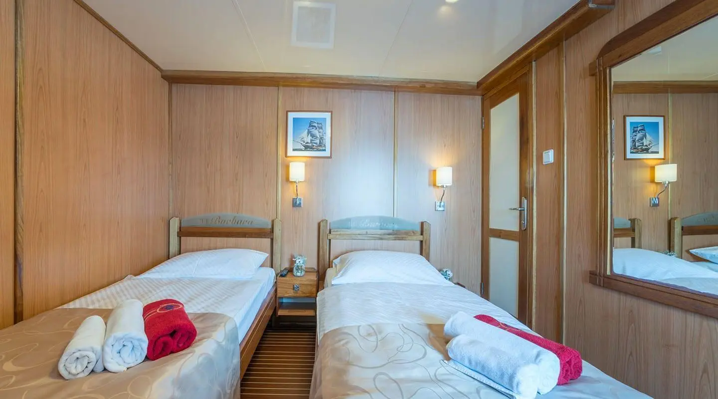 Interior of Barbara yacht: twin beds, wood paneling, bedside lamps, framed art