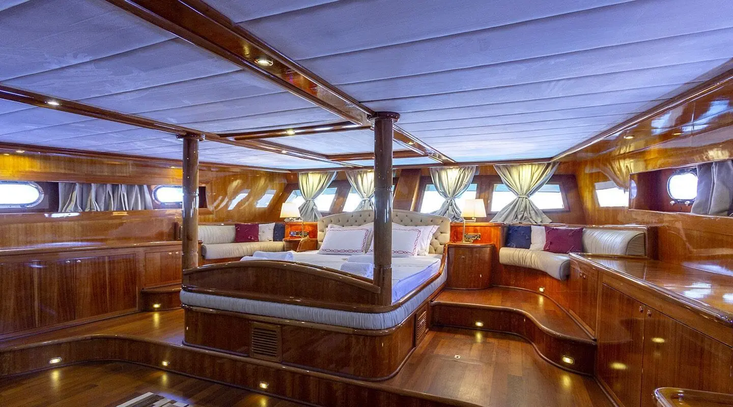 Interior of a luxury yacht with wooden deck, blue cushioned seating, and warm ambient lighting at sunset