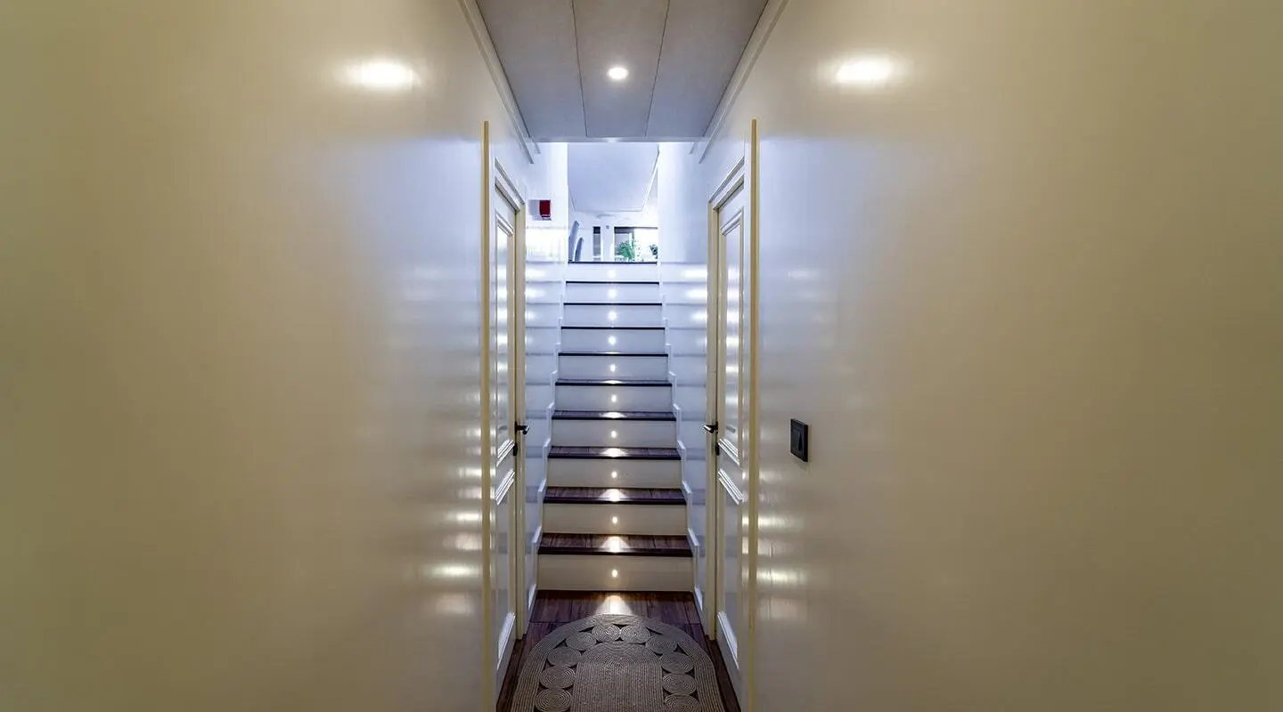Interior image of a narrow bright corridor with white glossy walls and stairs leading up