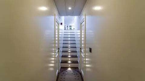 Interior image of a narrow bright corridor with white glossy walls and stairs leading up