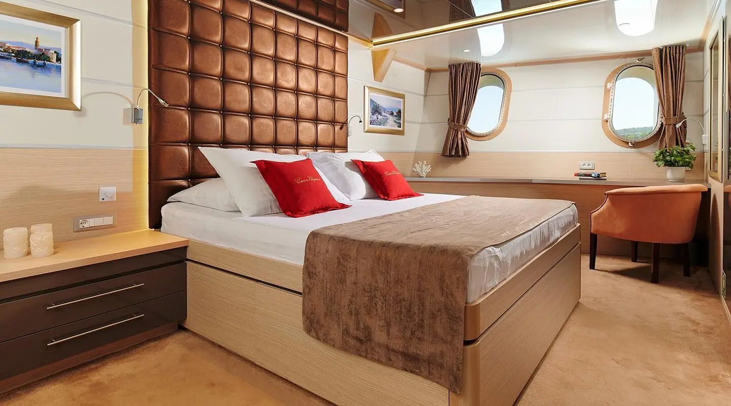 Queen Eleganza yacht interior: luxurious bed, red cushions, warm lighting