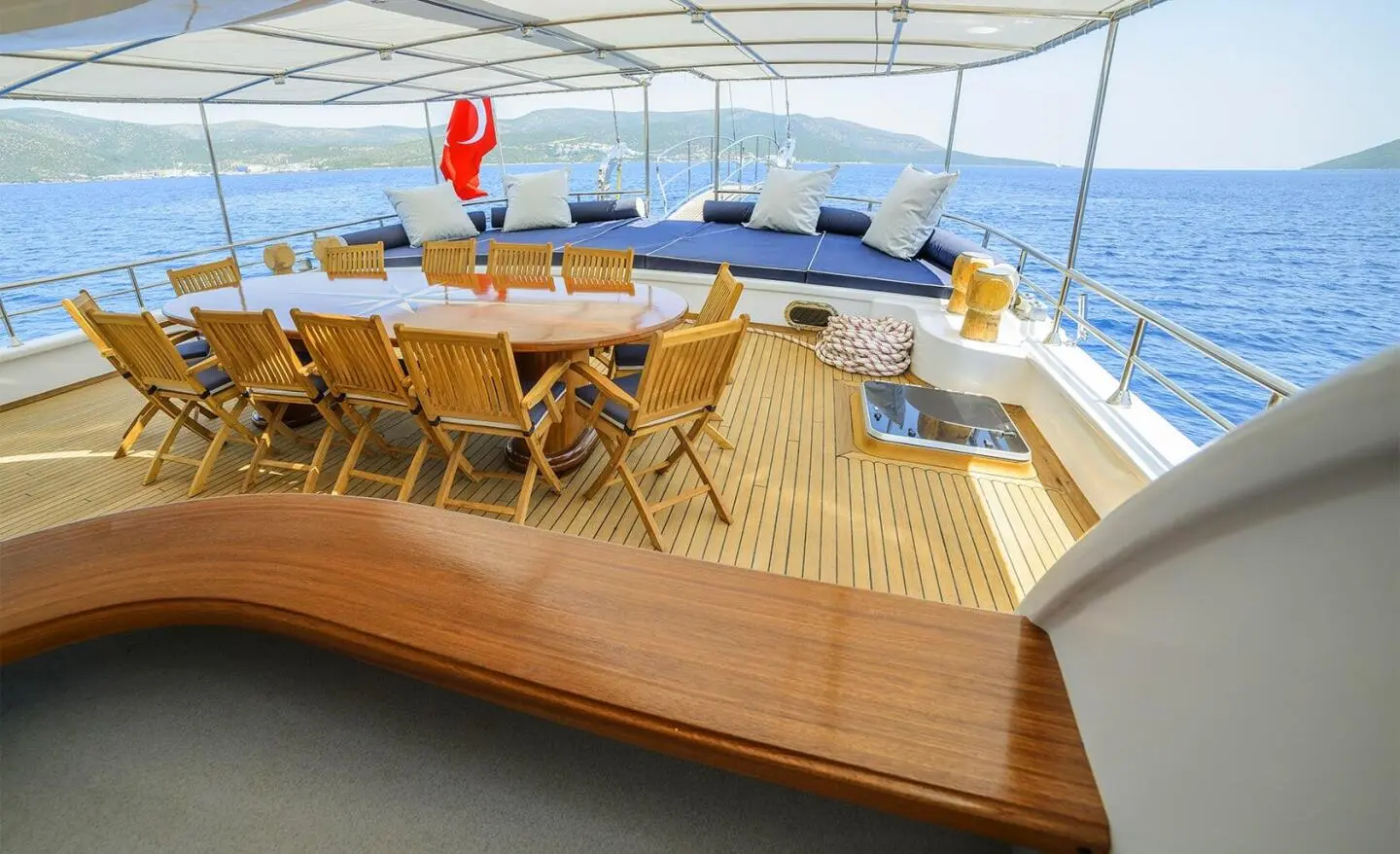 Bella Mare yacht deck with wooden seating, sun loungers, and blue cushions at sunset