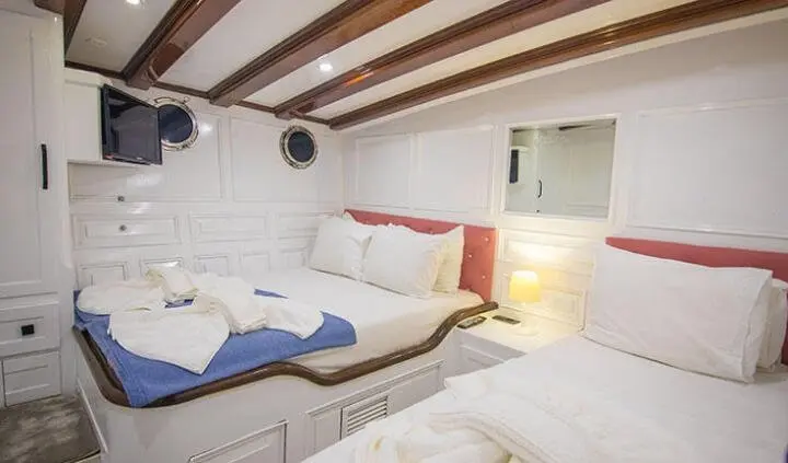 Double cabin with ensuite on Grande Mare yacht; white seating, blue cushions, wooden beams, compact cabin feel