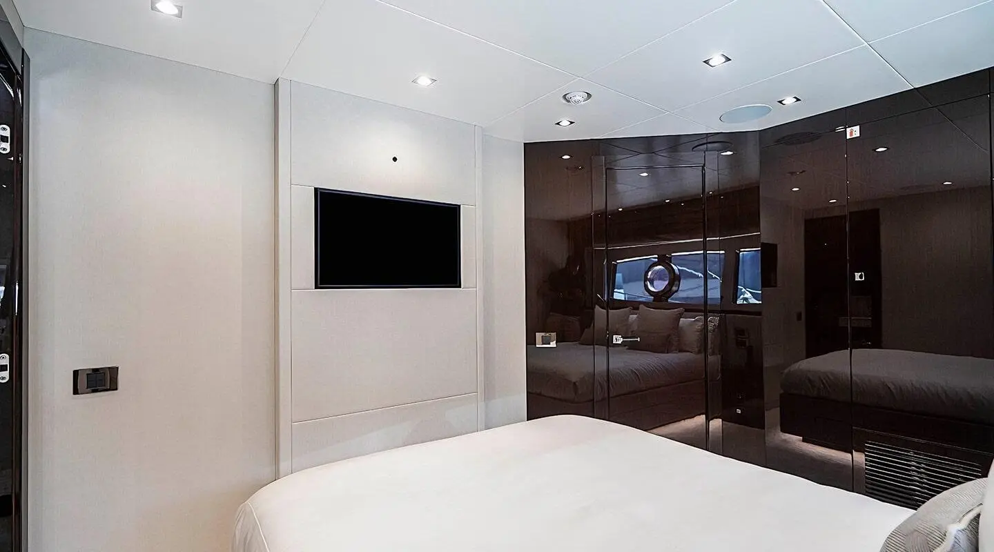 Interior of a bedroom with white walls, a wall-mounted TV, and a bed in view