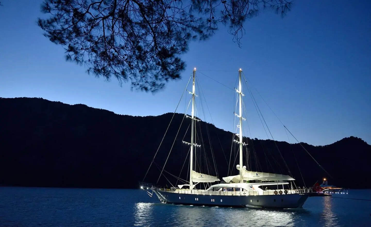 Gulet Alessandro I anchored at night with calm water and hills in the background