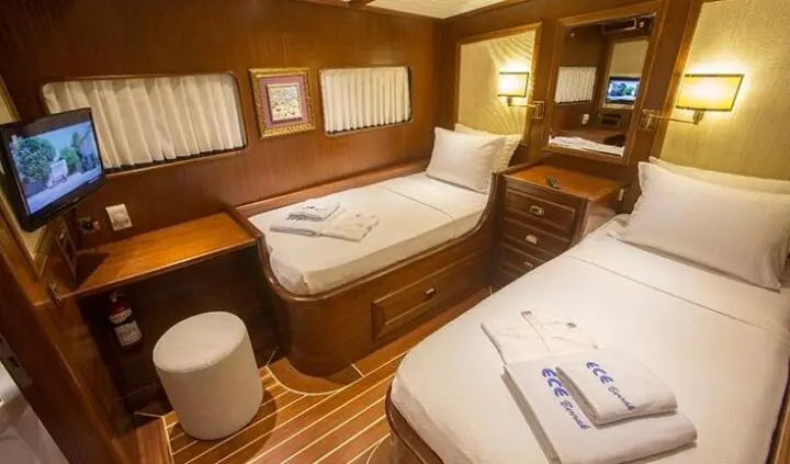 Twin cabin on yacht with two single beds, wood paneling, warm lighting