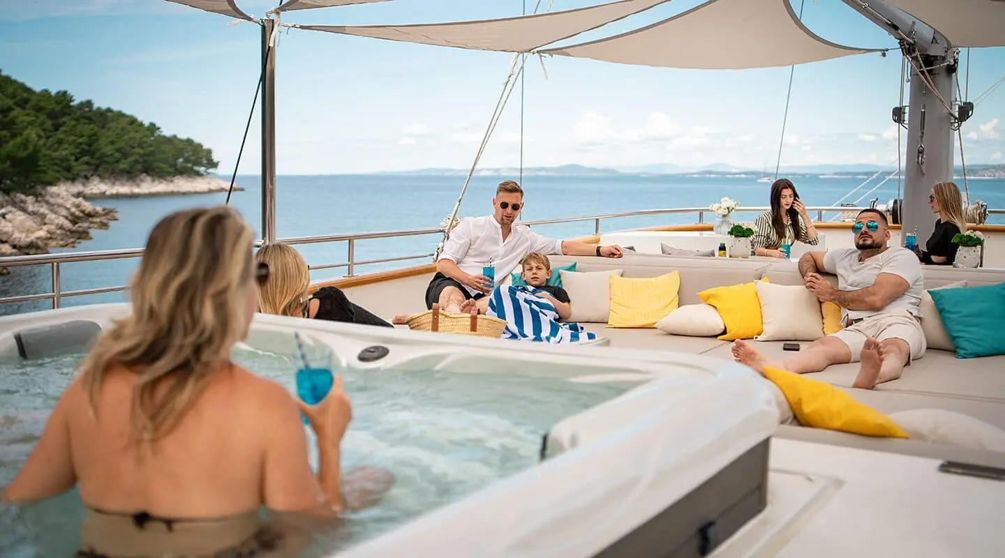 Dalmatino yacht sun deck with people relaxing in a hot tub under shade sails