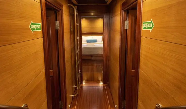View down a wooden yacht hallway toward a brighter cabin with metal framed doorways