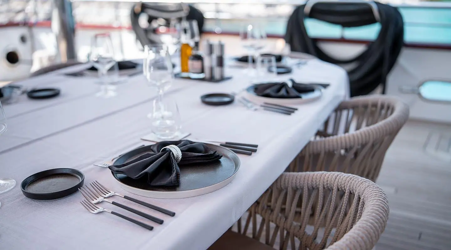 Nocturno yacht dining on deck with elegant table setting and black napkin centerpiece