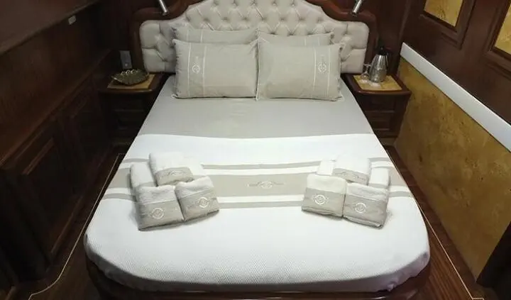 Double bed with white linens and two rolled towels at foot on yacht cabin