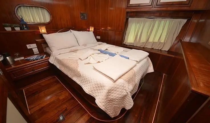 Master cabin with two single beds pushed together, white bedding, wooden walls, window with blinds