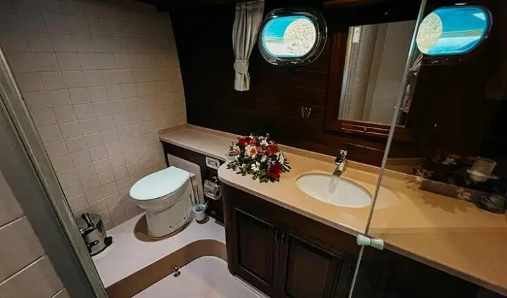 Small yacht cabin with wooden cabinets, sink, porthole window, and mirror