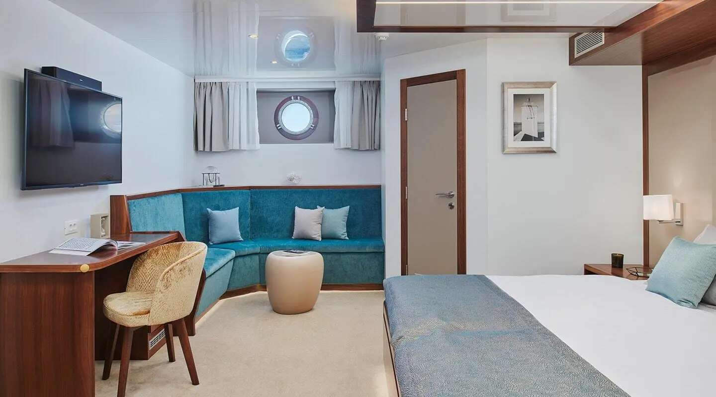 Corsario yacht interior with blue sofa, dining table, and windows at sunset