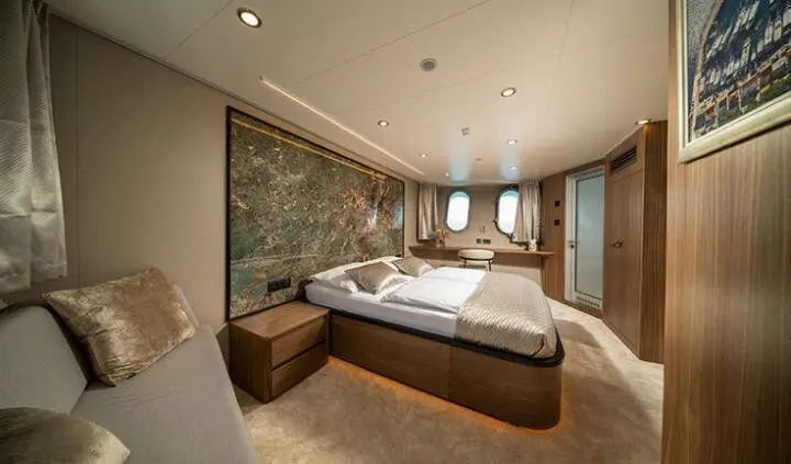 Interior of a yacht cabin with two beds, wooden accents, and ample lighting