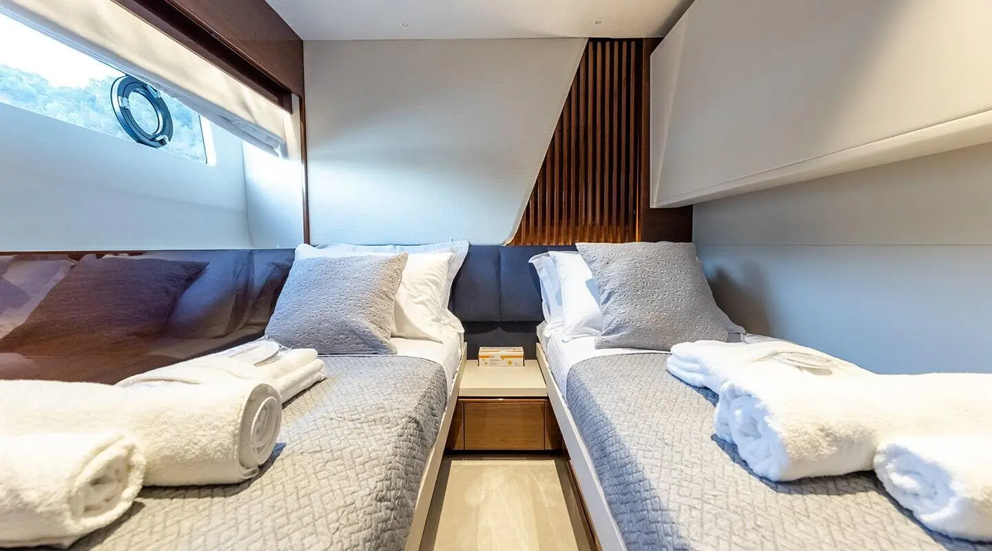 Vista yacht cabin with two single beds, porthole window, and neutral cushions