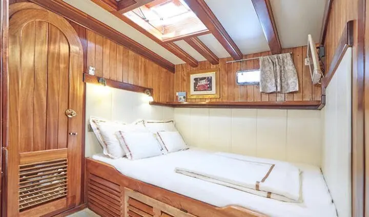 Yacht Libra cabin with two twin beds, wooden cabinetry, porthole light