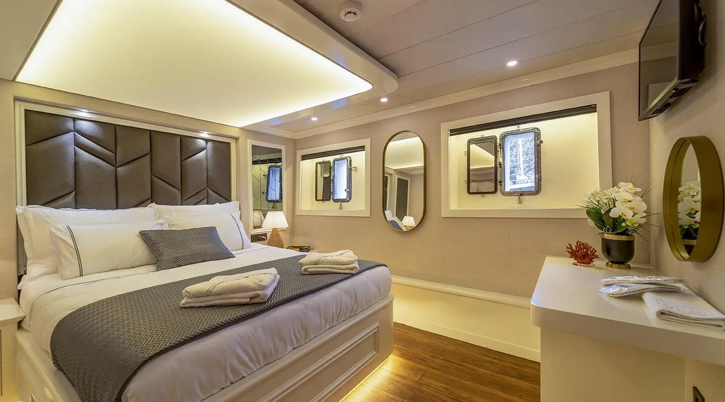 Queen Of Makri yacht interior with bed, lamps, and framed windows at sunset