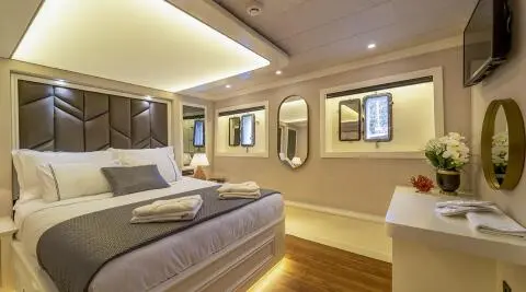 Queen Of Makri yacht interior with bed, lamps, and framed windows at sunset