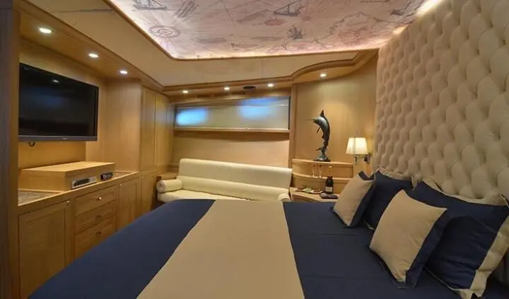 Yacht cabin with king bed, beige walls, blue bedding, bedside lamps, window view